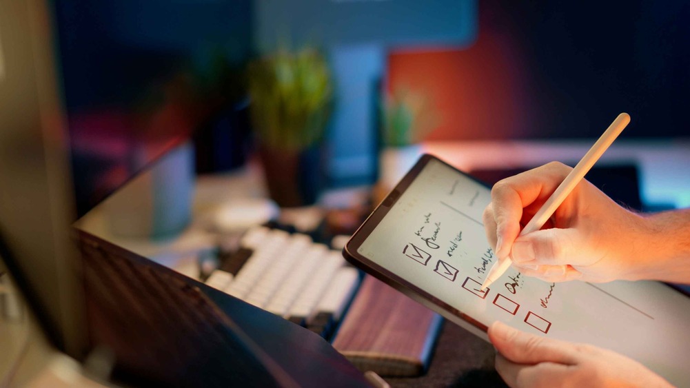 Close-up of a person checking items on a digital banker's checklist with a stylus in a dimly lit office setting.